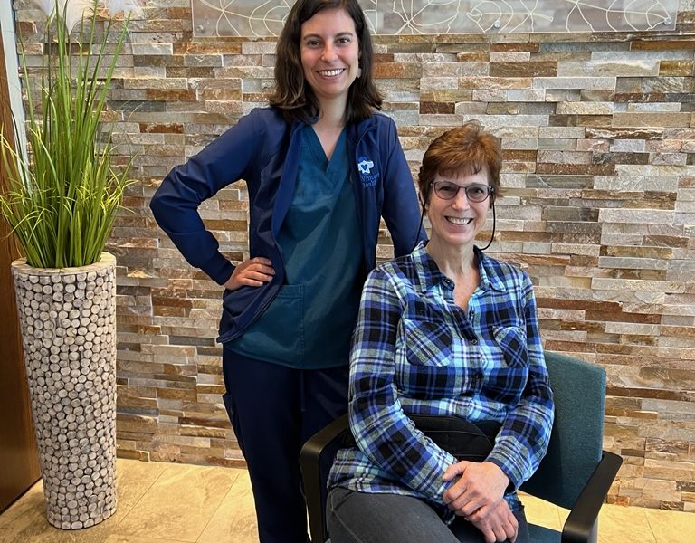 Wound Care nurse, Lindsy Coon (standing) is pictured with her patient Marianne Maes (sitting) in front of the St. Vincent Health Logo wall.